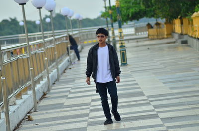 Young man wearing sunglasses walking on footbridge by railing
