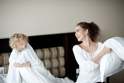 Happy mother and daughter playing pillow fight in bedroom