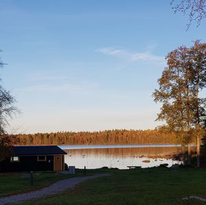 House on field by lake against sky