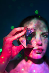 Close-up portrait of woman holding colorful over black background