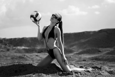 A young volleyball player girl in a bikini sitting on the sand with a ball, beach volleyball