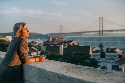 Man standing on bridge looking at city against sky