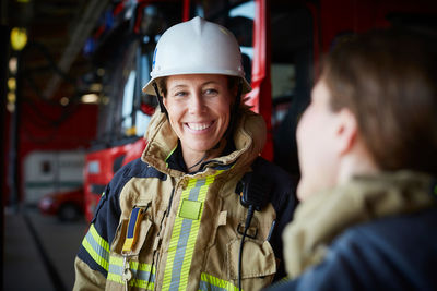 Smiling female firefighter looking at coworker in fire station