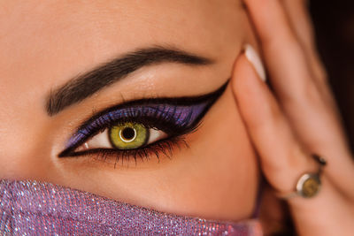 Woman eye with fancy arrow make-up under neon light. lady in glitter protective mask.