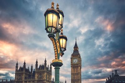 Low angle view of illuminated street light with big ben and houses of parliament against cloudy sky