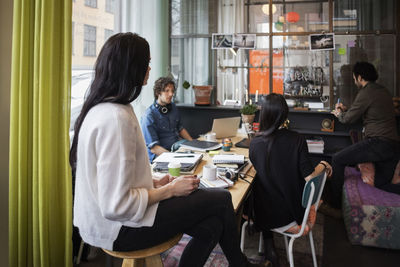 Creative team looking at man writing in adhesive note at modern office