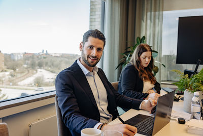 Portrait of smiling businessman sitting with colleague at desk in coworking office