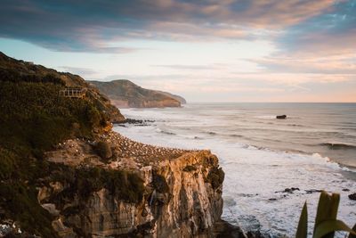 Scenic view of sea by cliff against cloudy sky