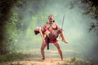 Full length of shirtless man standing in forest