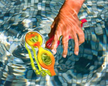 Cropped hand of child holding swimming goggles in pool