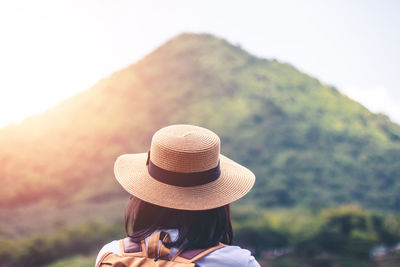 Rear view of woman holding hat against mountain