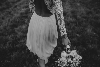 Low section of woman holding bouquet while walking on field