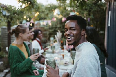 Side view portrait of smiling young man having fun with friends at party in back yard