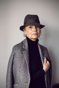 Fashionable older woman in black clothes and a hat stands against a white wall in the office