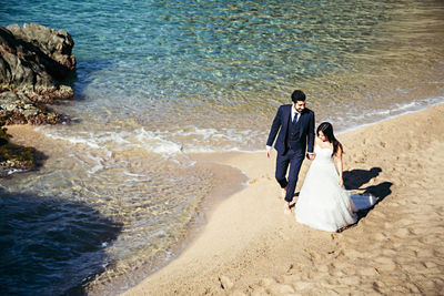 High angle view of newlywed couple walking at beach during sunny day