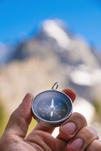Man holds a compass in his hand against the backdrop of mountains, blurred background, close-up