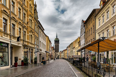 Empty road amidst buildings in city against sky