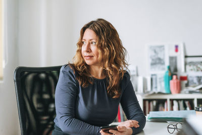 Charming smiling adult woman middle aged woman with curly hair designer in bright modern office