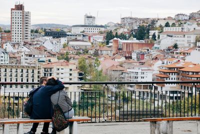 Rear view of couple sitting on bench against city