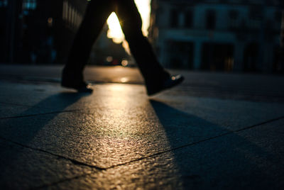 Low section of person walking on footpath during sunset