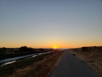 Road amidst field against clear sky during sunset