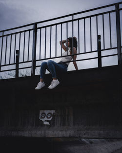 Low angle view of woman sitting on bridge