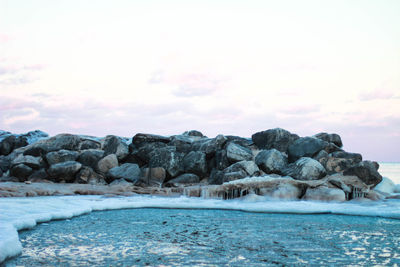 Rocks in sea against sky during sunset