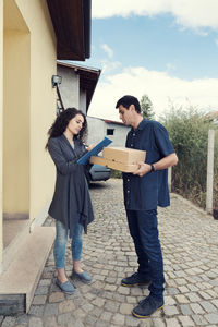 Woman signing on clipboard by delivery man against house