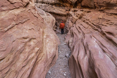 Tourist in outerwear with backpack standing near rough sandstone walls of little wild horse canyon during trip in utah, california