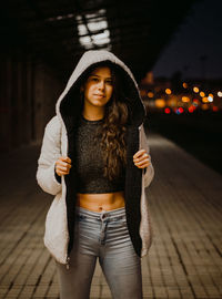 Portrait of beautiful young woman standing against wooden wall at night