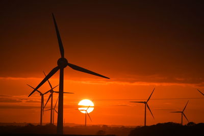 Silhouette wind turbines on field against sky during sunset