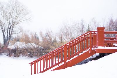 Footbridge over snow covered field against sky