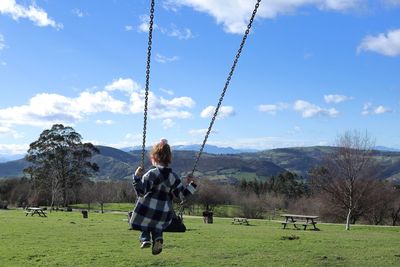 Girl on swing on field against sky