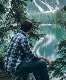 Side view of young man looking at lake with mountain reflection