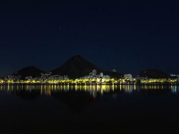 Illuminated city by sea against sky at night