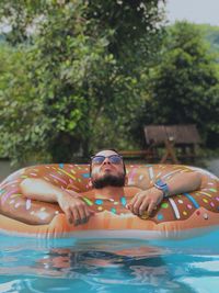 Mid adult man wearing sunglasses with inflatable ring swimming in pool