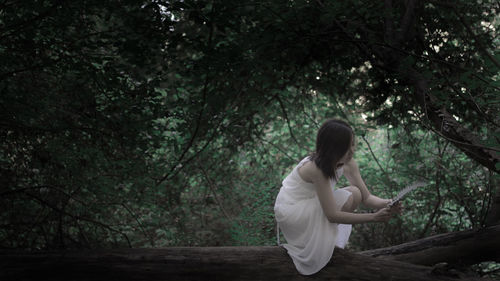 Side view of woman sitting in forest