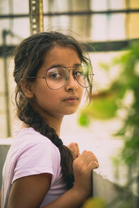 Portrait of girl wearing eyeglasses standing by retaining wall 