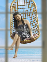 Close-up portrait of smiling young woman sitting on swing at beach