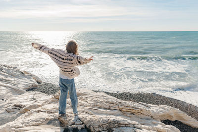 Teenage girl with arms outstretched looking at sea standing on rock at beach