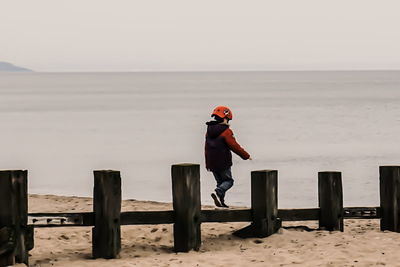 Child walking by jetty at beach against sky