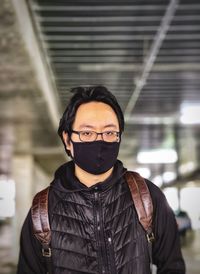 Portrait of young man in face mask standing against ceiling and wall.