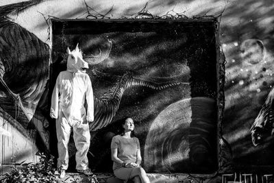 Woman sitting by person wearing horse costume against wall