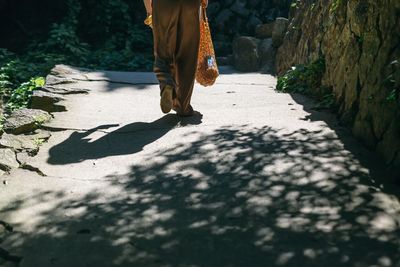 Low section of man walking on footpath during sunny day