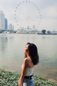 Young woman looking away standing by sea in city