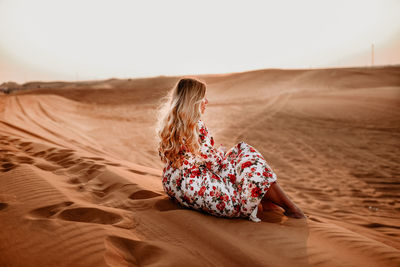 Man sitting on sand dune in desert against sky