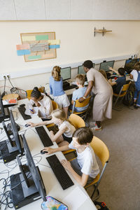 High angle view of male and female pupils with teacher in computer class at school