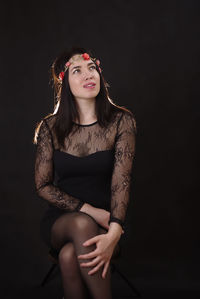 Smiling beautiful woman wearing wreath while sitting against black background