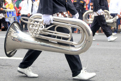 Low section of man holding saxophone while walking on road