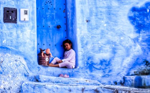 Full length of boy sitting against blue wall